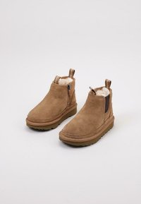 Botines de ante marrón con un forro suave, cierre de cremallera lateral y lengüeta. Suela de goma gruesa con detalles de costura.
