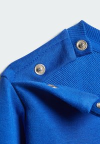 Detalle de una prenda de punto azul con un cuello acanalado, botones a presión plateados y una textura suave. La tela es vibrante y de tejido ajustado.