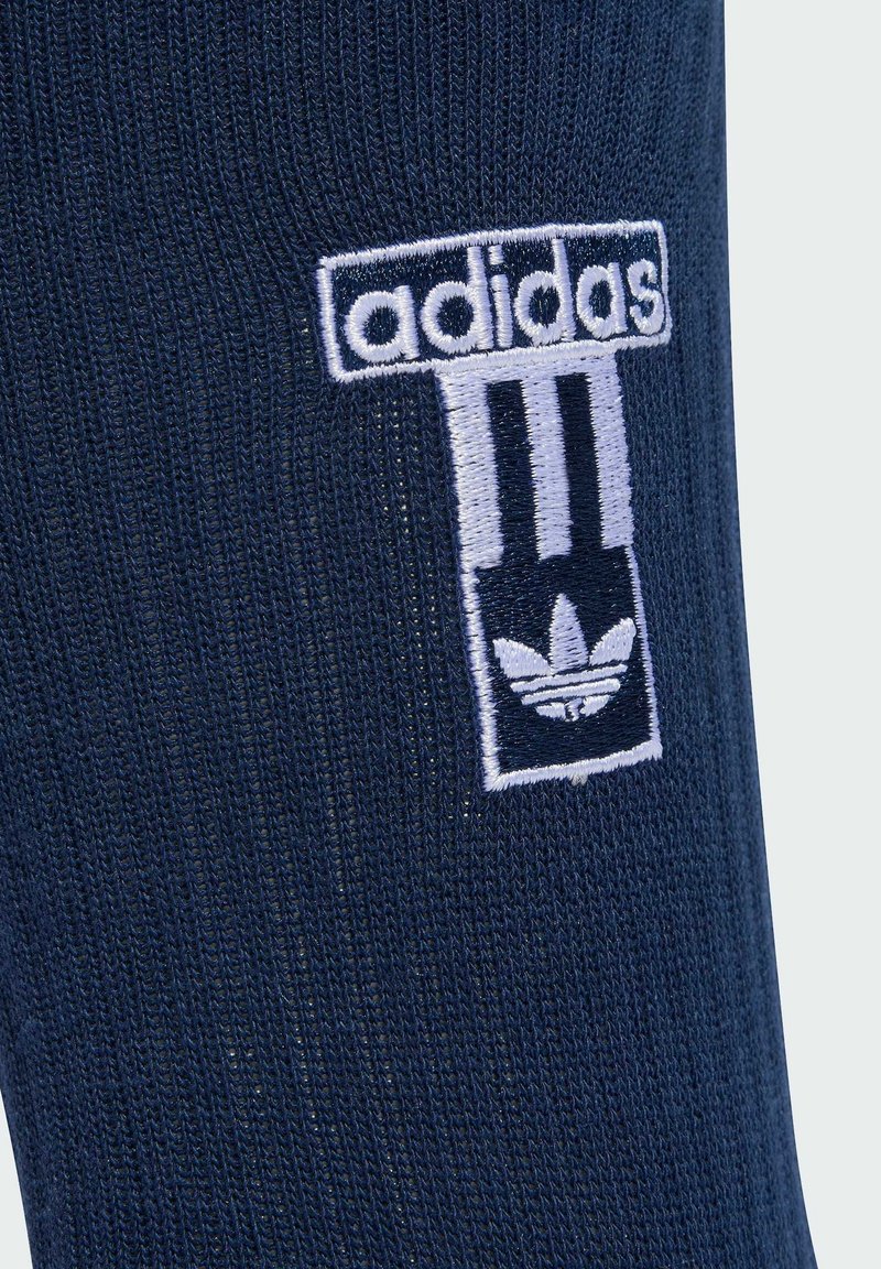 Calza blu navy con logo Adidas ricamato in bianco, caratterizzato da tre strisce e trefoil nella parte inferiore, realizzata in materiale a maglia testurizzata.