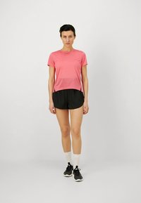 Rövid, rózsaszín sportpóló könnyű anyagból, fekete rövidnadrággal párosítva. A modell fehér zoknit és fekete tornacipőt visel, egyenesen áll.