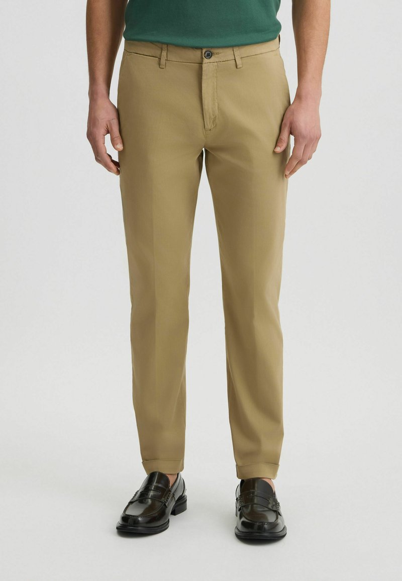 Katoenen tan broek met een rechte snit, voorzien van een knoopsluiting en riemlussen, gecombineerd met zwarte leren instappers.