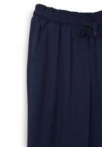 Pantalon en tissu léger bleu marine avec une ceinture élastique, un cordon de serrage et des poches latérales. Texture lisse avec une coupe décontractée.
