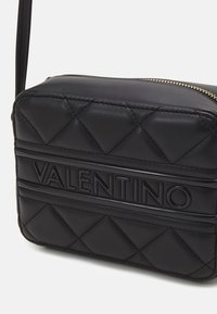 Černá prošívaná kožená kabelka přes rameno se zlatým zipem a vyvýšeným logem VALENTINO na předním panelu.
