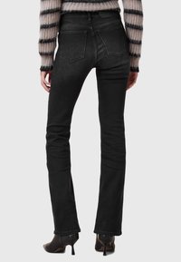 Jeans neri aderenti con una texture liscia, caratterizzati da un alto punto vita, tasche posteriori e cuciture sottili. Completati da scarpe con tacco.