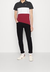 Polohemd mit schwarzen, weißen und marsala horizontalen Streifen; kombiniert mit schwarzen Slim-Fit-Hosen und weißen Turnschuhen mit roten Akzenten.