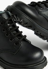Schwarze Lederstiefel mit runder Zehenpartie, strukturiertem Obermaterial, schwarzen Schnürsenkeln und robustem Gummisohle mit ausgeprägtem Profil.