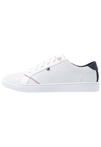 Białe trampki z teksturowaną cholewką, ozdobione małym logo, czerwonymi i niebieskimi akcentami oraz granatowym zapiętkiem. Posiadają białą gumową podeszwę i sznurówki.