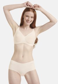 Beige saumatön pitot ja alushousut, jotka on valmistettu pehmeästä kankaasta. Pitovassa on säädettävät olkaimet ja sileä pinta. Alushousut ovat minimalistisessa designissa.
