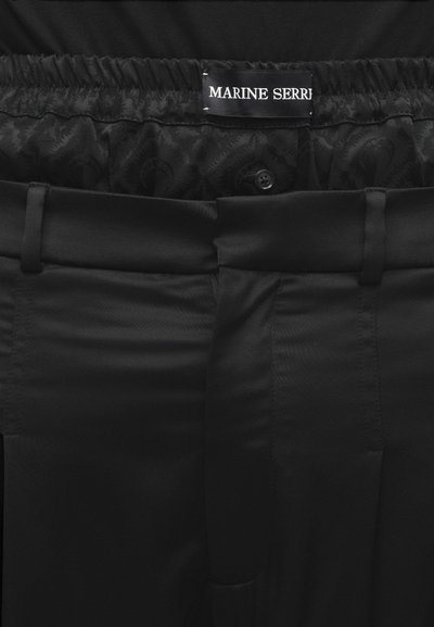 Μαύρο παντελόνι με υφασμάτινη μέση με ανάγλυφο σχέδιο, κλείσιμο με κουμπί και ετικέτα «MARINE SERRE». Λείο ύφασμα με τσέπες στο μπροστινό μέρος.