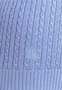 Suéter de punto azul claro que presenta un diseño de trenzado texturizado, dobladillo acanalado y un logo bordado en el lado inferior.