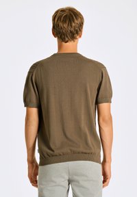 Kortärmad brun stickad tröja med ribbade manschetter och nederkant. Har texturerad detalj vid axlarna och en figurnära design vid midjan.