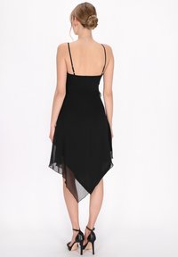 Fekete ruha vékony pántokkal, folyamatos, a háta felé pontig szűkülő hemline-nel. Sima textúra és könnyű anyag.