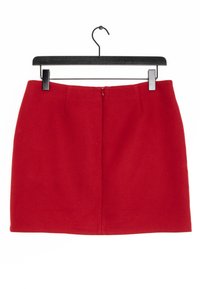 Jupe rouge en tissu texturé, dotée d'une fermeture éclair dissimulée au dos et de deux plis à l'avant pour plus de détail. Accrochée à un cintre noir.