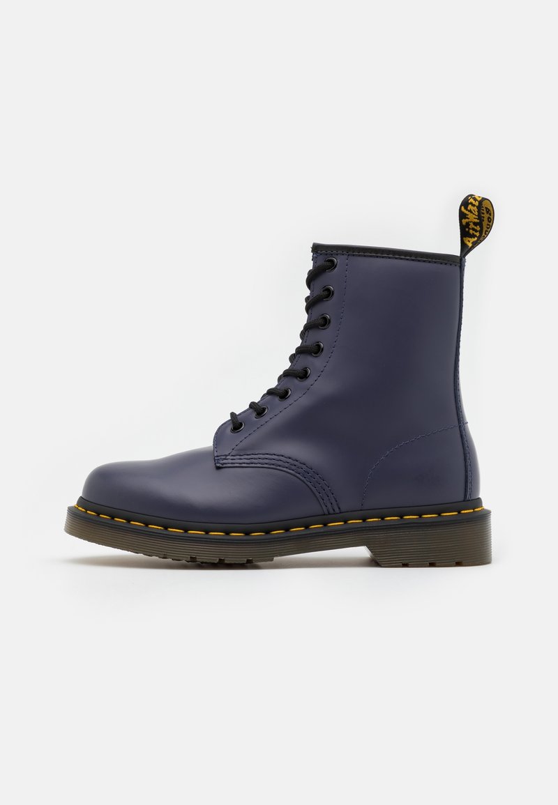 Bottine en cuir bleu marine à lacets, avec surpiqûres jaunes, semelle noire et languette de traction siglée au talon.