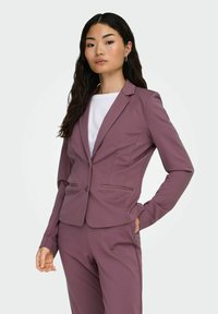 Skreddersydd lilla blazer i stretchy stoff, med klaffeslag, to frontlommer, og en figursydd design med subtile søm detaljer.