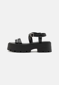 Black platform sandals with a chunky sole, featuring two straps across the foot and an ankle strap with a metal buckle. Smooth texture.