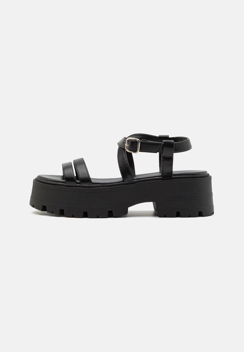 Black platform sandals with a chunky sole, featuring two straps across the foot and an ankle strap with a metal buckle. Smooth texture.