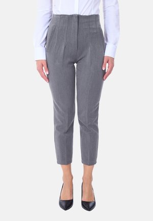 Pantaloni grigi su misura con pieghe, lunghezza corta, realizzati in un tessuto testurizzato. Indossati con una camicia bianca a bottoni e tacchi neri.