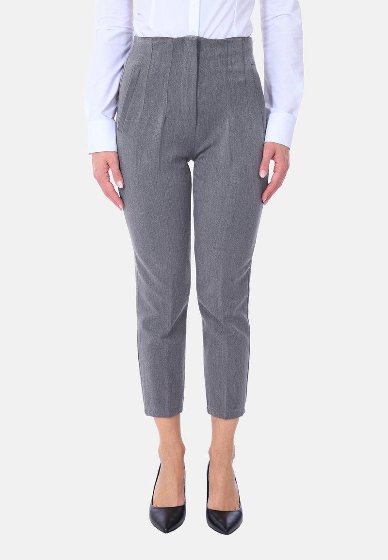 Pantaloni grigi su misura con pieghe, lunghezza corta, realizzati in un tessuto testurizzato. Indossati con una camicia bianca a bottoni e tacchi neri.