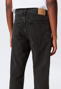 Calças de ganga pretas com corte direito, design de cinco bolsos e uma etiqueta de couro castanho com a marca na parte de trás da cintura.