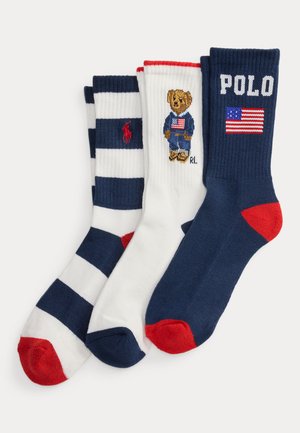Trzy złożone skarpetki w kolorach granatowym, białym i czerwonym; paskowana skarpetka, biała skarpetka z misiem trzymającym flagę oraz granatowa skarpetka z napisem "POLO" i flagą amerykańską.