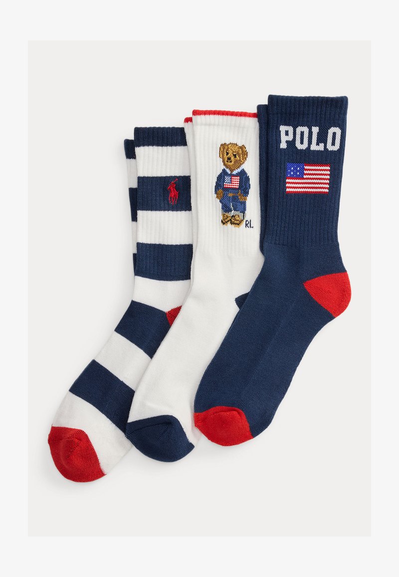 Τρία διπλωμένα καλτσάκια σε ναυτικό μπλε, λευκό και κόκκινο· ριγέ κάλτσα, λευκή κάλτσα με αρκούδα που κρατάει σημαία, και ναυτικό μπλε κάλτσα με τη λέξη «POLO» και την αμερικανική σημαία.
