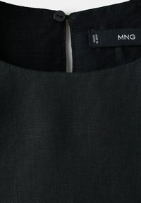 Encolure d'un vêtement en lin noir avec fermeture à bouton et étiquette de la marque MNG cousue à l'intérieur, l'étiquette indique également fabriqué en Chine.