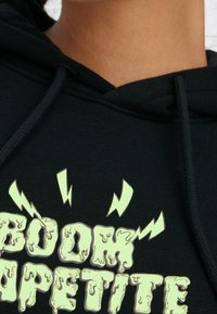 Sudadera negra con un gráfico que presenta el texto "BOOM APPETITE" en verde claro, con un efecto goteante y acentos de relámpago.