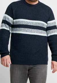 Maglione a coste blu con strisce orizzontali in azzurro chiaro e bianco sul petto. Maniche lunghe e scollatura rotonda.