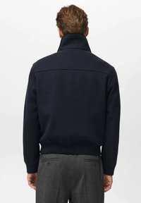 Giacca a pullover blu navy con collare alto, polsini e orlo a costine. Caratterizzata da una texture liscia e da un design pulito e minimalista.