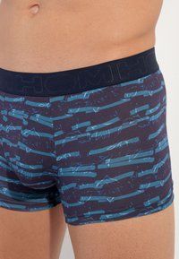 Boxer briefs made of stretchy jersey fabric, featuring a navy background with blue horizontal stripes and leaf patterns. Elastic waistband.