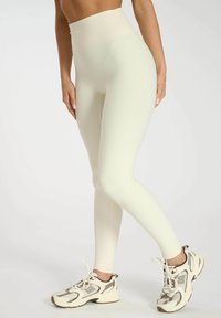 Leggings côtelés taille haute, jaune clair, avec une texture lisse, associés à des baskets de sport blanches et marron.