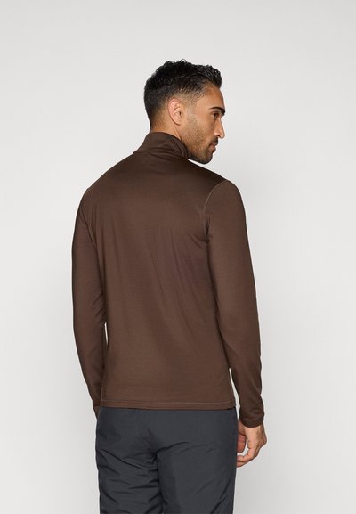 Brun långärmad topp med hög krage, tillverkad av ett slätt tyg. Har minimala sömnadsdetaljer och en figurnära design.