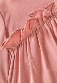 Różowy materiał o teksturowanej powierzchni, z marszczonym brzegiem i zbieraną nicią. Projekt podkreśla miękkość i delikatne kontury.