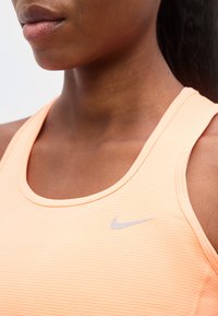 Κοντινό πλάνο ενός ατόμου που φοράει ένα ροδακινί αμάνικο αθλητικό τοπ με μικρό γκρι λογότυπο Nike στο στήθος.