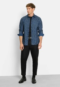 Herrenhemd mit langen Ärmeln in Dunkelblau mit floralem Muster, kombiniert mit schwarzen Hosen und schwarzen Schuhen für einen klassischen, maßgeschneiderten Look.