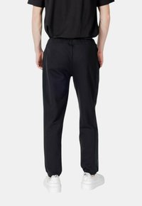 Schwarze Sweatpants mit elastischem Bund, seitlichen Taschen und Streifen an den Seiten. Kombiniert mit weißen Sneakers. Weicher Stoff mit glatter Textur.