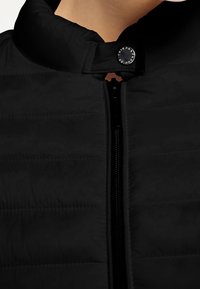 Close-up of zipped black quilted jacket with snap button collar on a person’s neck and upper chest area.