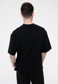 Black short-sleeve T-shirt with a loose fit, crew neck, and smooth cotton texture. Simple design with no visible patterns or accents.
