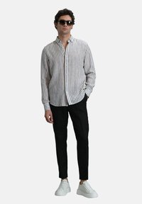 Gestreepte button-up shirt in lichtbeige en bruin, gecombineerd met zwarte broeken en witte sneakers. Zonnebrillen maken de outfit compleet.