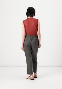 Top sin mangas en color óxido acompañado de pantalones grises con cintura elástica. El conjunto se complementa con sandalias de color claro con cordones.