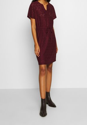 Bordowa sukienka z krótkim rękawem z wycięciem przy dekolcie, sznurkiem w talii, wzorzystą teksturą i długością przed kolano, zestawiona z czarnymi botkami za kostkę.