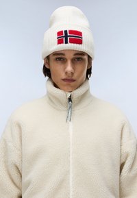 Cream fleece jacket with high collar and zip, paired with a knitted white beanie featuring a red and blue Norwegian flag design.