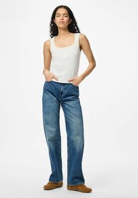 Top bianco a coste con scollo quadrato e dettagli di bottoni, abbinato a jeans a gamba larga blu chiaro con dettagli sbiaditi. Calzature marroni completano il look.