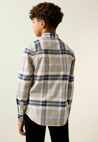 Camisa de cuadros en beige claro, azul y azul marino oscuro. Cuello abotonado, mangas largas con puños abotonados, dobladillo curvo y costura en el canesú trasero.