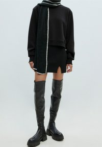 Sweat-shirt noir court associé à une mini-jupe noire côtelée avec une fente sur le devant. Bottes noires brillantes jusqu'aux genoux avec des semelles épaisses et des zips.