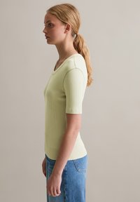 Lichtgroene geribde top met korte mouwen en een V-hals. Gecombineerd met blauwe denim jeans, die een aansluitende silhoeette tonen.