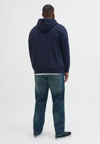Marineblå hættetrøje med snorhett, ribbet manchetter og kant, parret med falmede blå jeans og sorte sneakers. Simpel, afslappet design.