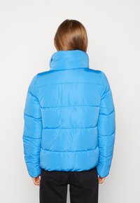 Veste rembourrée bleue avec un col haut, un design matelassé et des poignets élastiques. Texture lisse avec des détails de couture visibles.