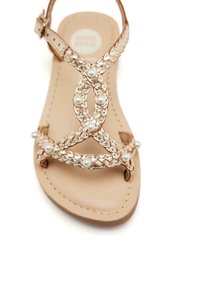 Sandalo beige con un design intrecciato e accenti di perle, suola piatta e cinturino con fibbia per la sicurezza. Artigianato semplice ed elegante.